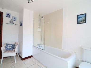 A bathroom with a bathtub and shower a white chair with cushions and wall decorations at The Corn Tallet in Westleigh near Bideford