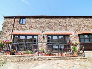 A stone house exterior with flower pots on a metal railing at The Corn Tallet in Westleigh near Bideford