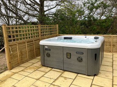 An outdoor hot tub on a tiled patio surrounded by wooden fencing and trees at The Corn Tallet in Westleigh near Bideford