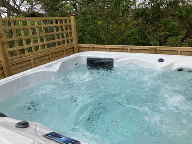 A bubbling hot tub with wooden privacy fencing and greenery in the background at The Corn Tallet in Westleigh near Bideford
