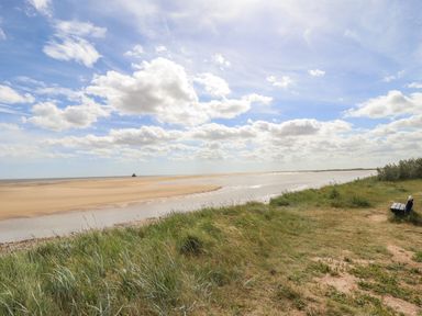 A sandy beach with water and grassy area with a bench near the shore at Rollin Dunes in Humberston Lincolnshire