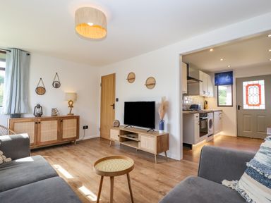 A living room with a grey sofa wooden sideboards a TV and an open door to the kitchen at Rollin Dunes in Humberston Lincolnshire