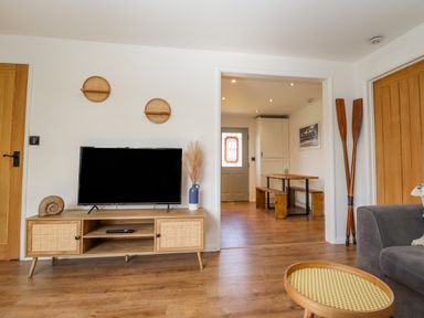 A living room with a TV on a wooden stand next to a doorway leading to a dining area with a wooden table and benches at Rollin Dunes in Humberston Lincolnshire