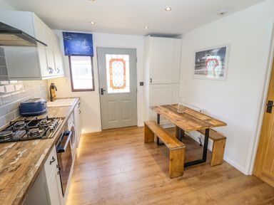A kitchen with wooden countertops a gas stove a blue toaster a wooden dining table with benches and a door with stained glass at Rollin Dunes in Humberston Lincolnshire