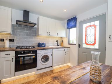A kitchen with white cabinets a gas stove oven washing machine wooden countertop and a door with stained glass at Rollin Dunes in Humberston Lincolnshire