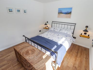 A bedroom with a bed a woven chest wooden floor and framed pictures at Rollin Dunes in Humberston Lincolnshire
