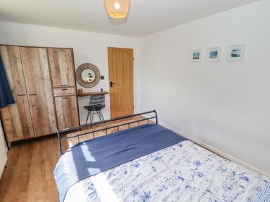 A bedroom with a bed covered with white and blue bedding a wooden wardrobe a small desk with a chair and a circular mirror on the wall at Rollin Dunes in Humberston Lincolnshire