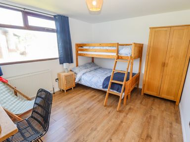 A bedroom with wooden bunk beds a wooden wardrobe a nightstand a lamp a black chair and a window with blue curtains at Rollin Dunes in Humberston Lincolnshire