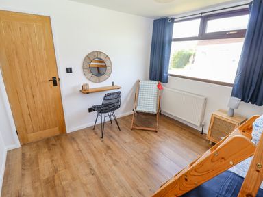 A room with a wooden door a black metal chair a folding chair a small wooden cabinet with a lamp and a window with dark curtains at Rollin' Dunes in Humberston Lincolnshire