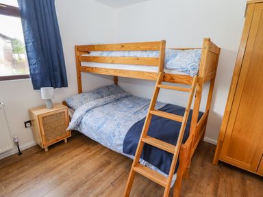 A bedroom with a wooden bunk bed blue bedding wooden wardrobe and a small wooden nightstand with a lamp at Rollin Dunes in Humberston Lincolnshire