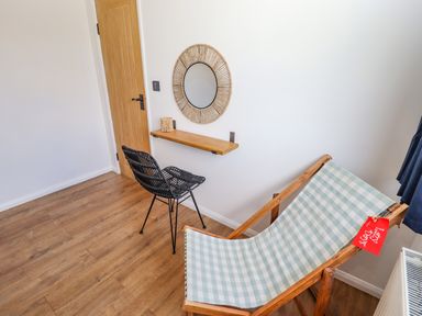 A room with a wooden door black chair small wall shelf round woven mirror and a folding deck chair at Rollin Dunes in Humberston Lincolnshire
