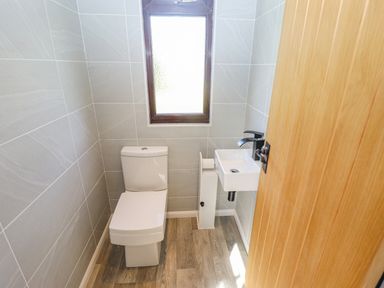 A small bathroom with a toilet a small sink a window and a wooden door at Rollin Dunes in Humberston Lincolnshire