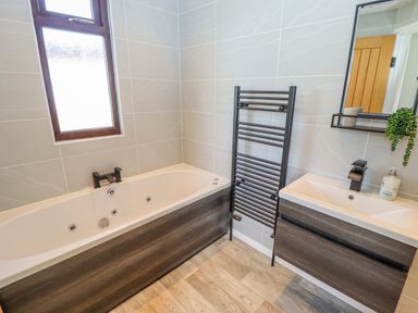 A bathroom with a bathtub sink mirror towel radiator and wooden floor at Rollin Dunes in Humberston Lincolnshire