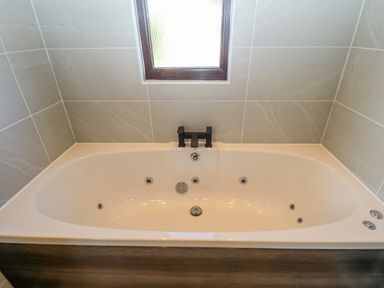 A bathtub with jets and a black faucet under a frosted window in a tiled bathroom at Rollin Dunes in Humberston Lincolnshire