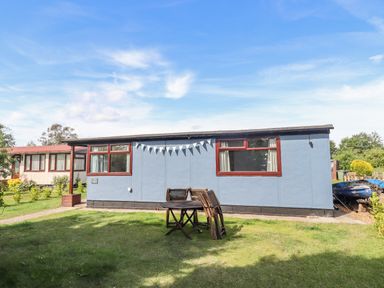 A single-story blue building with red windows and a wooden table with chairs on a grassy lawn at Rollin Dunes in Humberston Lincolnshire