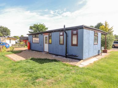 A small blue single-story building with multiple windows and a white door on a grassy plot at Rollin Dunes in Humberston Lincolnshire