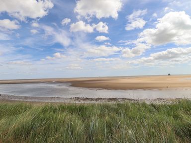 A coastal landscape with sand, water, and grassy dunes under a cloudy blue sky at Rollin Dunes in Humberston Lincolnshire