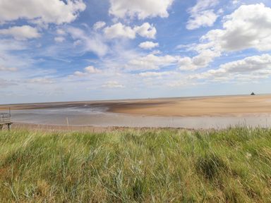 A sandy beach with tidal pools and grassy foreground under a partly cloudy sky at Rollin Dunes in Humberston Lincolnshire