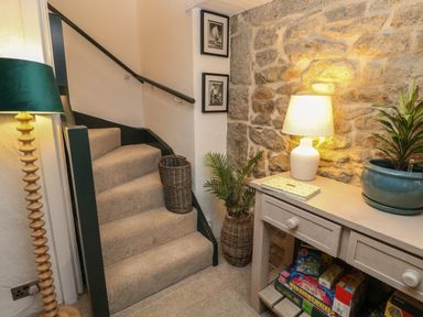 A carpeted staircase next to a wooden table with a lamp a plant and board games at Wood Brook Cottage in Crowan
