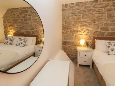 A bedroom with a bed pillows nightstand with lamp and stone wall at Wood Brook Cottage in Crowan