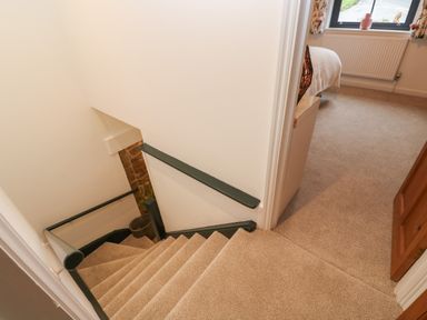 A carpeted staircase with green handrails leading down to a lower floor and a bedroom with a bed and window at Wood Brook Cottage in Crowan