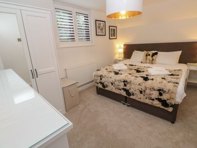 A bedroom with a bed covered with a spotted blanket and pillows two bedside tables with lamps a wardrobe and a window with shutters at Wood Brook Cottage in Crowan