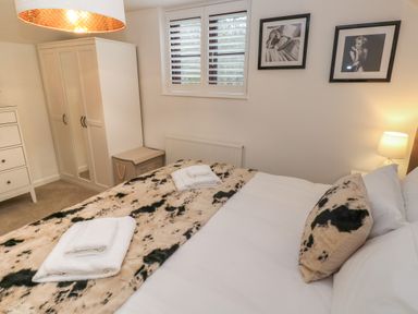 A bedroom with a bed covered in patterned bedding towels on the bed a wardrobe next to a window with shutters framed black and white photos on the wall at Wood Brook Cottage in Crowan
