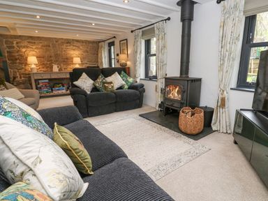 A living room with sofas cushions a wood burning stove and a console with board games at Wood Brook Cottage in Crowan