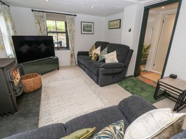 A living room with a black sofa a television a wood stove and a woven basket at Wood Brook Cottage in Crowan