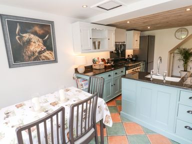 A kitchen with a dining table with candles a painting of a bull cabinets and a plant at Wood Brook Cottage in Crowan