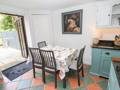 A dining area with a table covered by a printed tablecloth and four chairs next to open glass doors at Wood Brook Cottage in Crowan