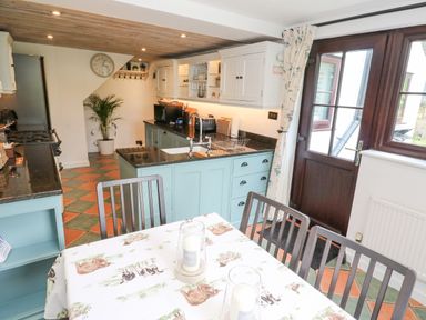 A kitchen with a dining table and chairs a stove and sink cabinets and a door leading outside at Wood Brook Cottage in Crowan