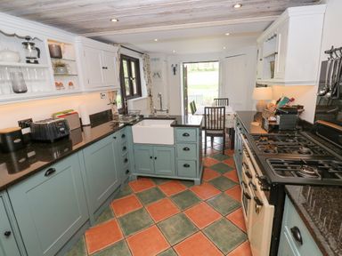 A kitchen with blue cabinets black countertops a white sink and a gas stove at Wood Brook Cottage in Crowan