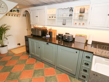 A kitchen with a green base cabinets black countertop white upper cabinets and a tiled floor at Wood Brook Cottage in Crowan