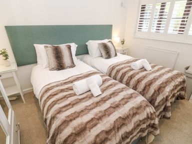 A bedroom with two single beds with brown striped blankets and white rolled towels at Wood Brook Cottage Crowan