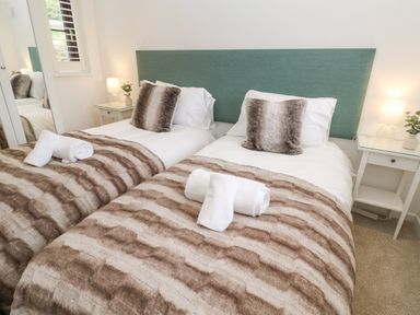 A bedroom with two single beds each with a striped blanket and a fur pillow at Wood Brook Cottage in Crowan