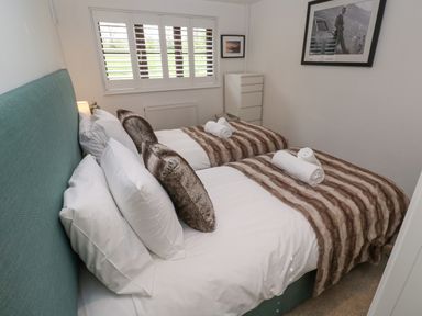 A bedroom with two single beds made up with white linens and brown striped throws at Wood Brook Cottage in Crowan