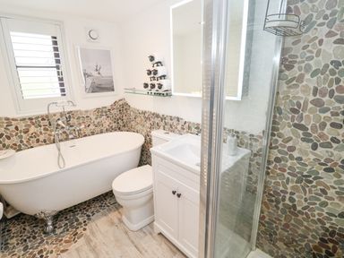 A bathroom with a bathtub toilet sink and a shower with pebble stone walls and wooden floor at Wood Brook Cottage in Crowan