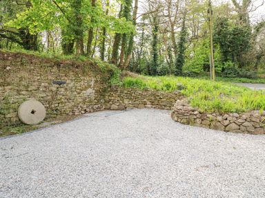 A gravel driveway with stone walls and greenery at Wood Brook Cottage in Crowan