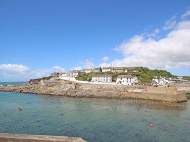 A coastal village with houses on a hill overlooking a harbor with a stone pier and clear water at Wood Brook Cottage in Crowan