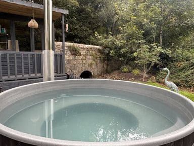 A hot tub with a flue pipe and stone wall at Wood Brook Cottage in Crowan