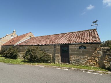 A stone cottage with a tiled roof bushes and a horse weather vane at Beaconsfield Cottage in Burniston near Scalby