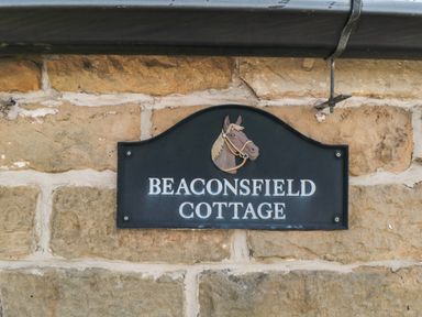 A black sign with a horse head illustration and the text Beaconsfield Cottage on a stone wall at Beaconsfield Cottage in Burniston near Scalby