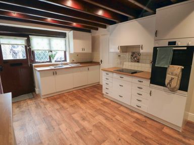A kitchen with wooden floor, white cabinets, a stove, oven and a door with windows at Beaconsfield Cottage in Burniston near Scalby