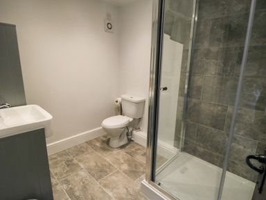 A bathroom with a toilet sink and a shower with glass doors and tiled walls at Beaconsfield Cottage in Burniston near Scalby
