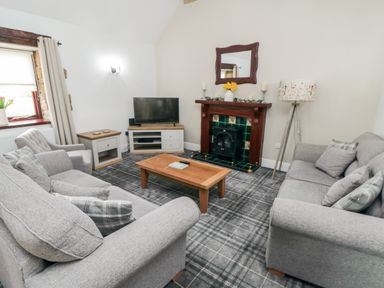 A living room with two grey sofas a tv on a stand a wooden coffee table a fireplace with a mirror above and a lamp at Beaconsfield Cottage in Burniston near Scalby