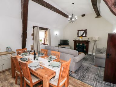 A dining table set for six with a bottle of wine in a living room with sofas a TV and fireplace at Beaconsfield Cottage in Burniston near Scalby
