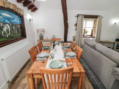 A dining table set with plates and glasses next to a gray sofa in a room with a stained glass window and wooden beams at Beaconsfield Cottage in Burniston near Scalby