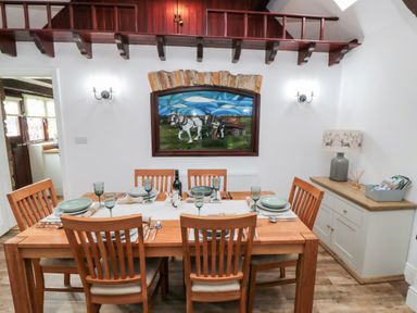 A dining room with wooden table and six chairs plates and glasses on the table a sideboard with lamp and box on top and a stained glass window at Beaconsfield Cottage in Burniston near Scalby