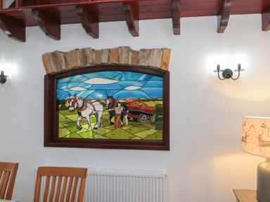A dining room with wooden chairs and a stained glass window depicting horses pulling a cart at Beaconsfield Cottage in Burniston near Scalby
